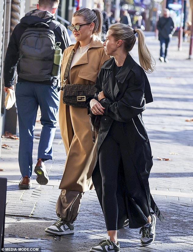 Emma se vistió con una gabardina igualmente elegante mientras tomaba un café con su amiga, que usaba zapatos Nike a juego.