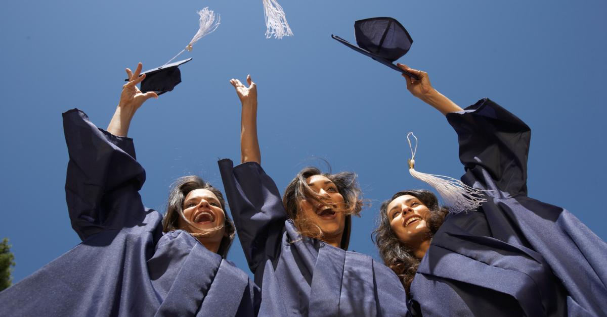 Tres graduadas universitarias lanzando sus gorras al aire.