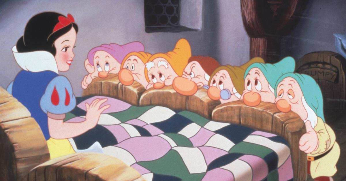 The seven dwarfs looking at Snow White as she sits in bed